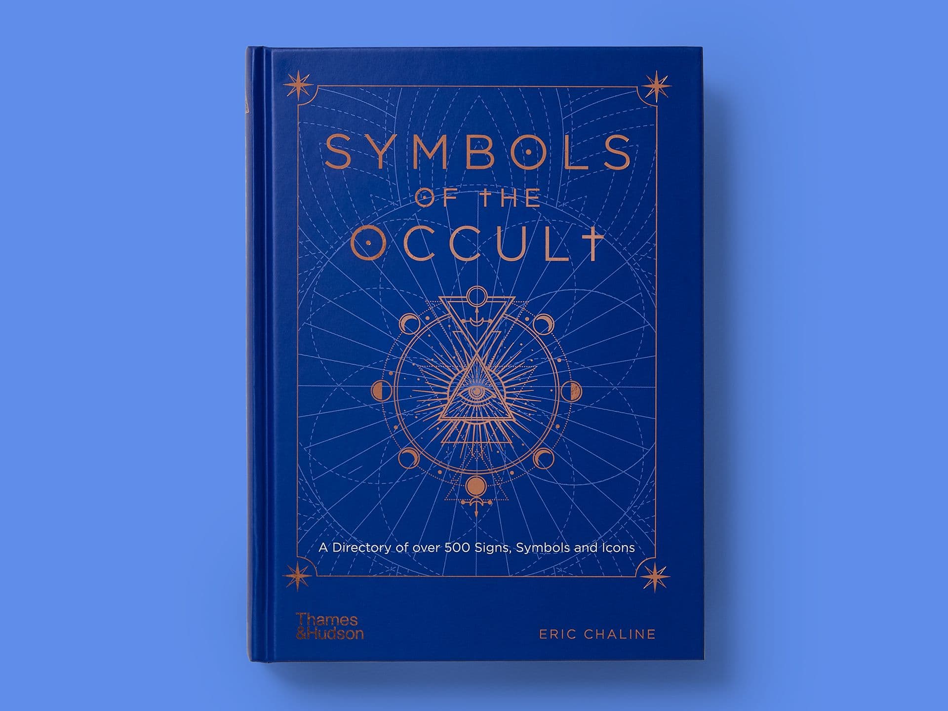 Book entitled "Symbols of the Occult" on a blue background. Deep blue cover with copper-foil geometric linework, celestial diagrams, and an all-seeing eye within a triangle at the centre. Title reads "Symbols of the Occult," subtitle notes a directory of over 500 signs, symbols, and icons, with author Eric Chaline credited below.