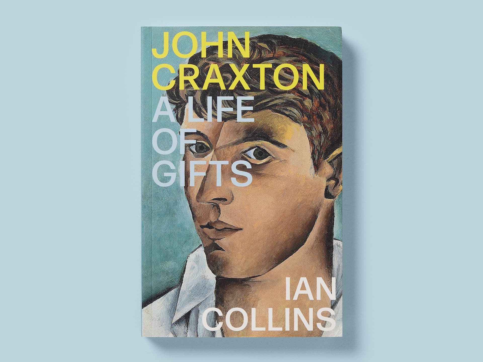 Book titled "John Craxton: A Life of Gifts" on a pale blue background, featuring a painted portrait on the cover. Bold yellow and white typography overlays the artwork, with the title and artist’s name at the top and author Ian Collins credited at the bottom.