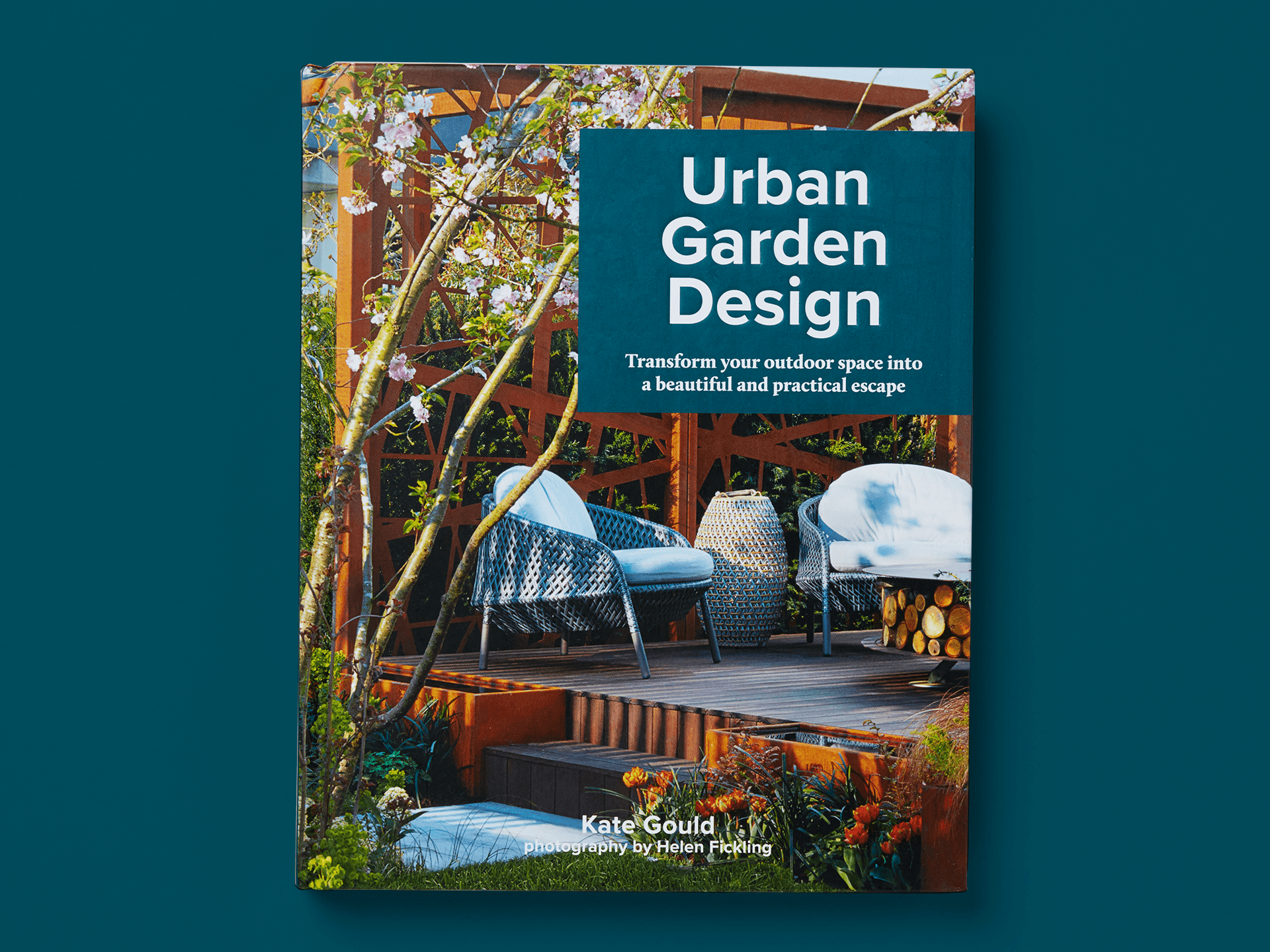 Urban garden scene on the cover of "Urban Garden Design", featuring a raised timber deck with woven outdoor chairs and cushions, planting, and flowering trees and greenery. Subtitle reads "Transform your outdoor space into a beautiful and practical escape," with author Kate Gould and photography credit to Helen Fickling.