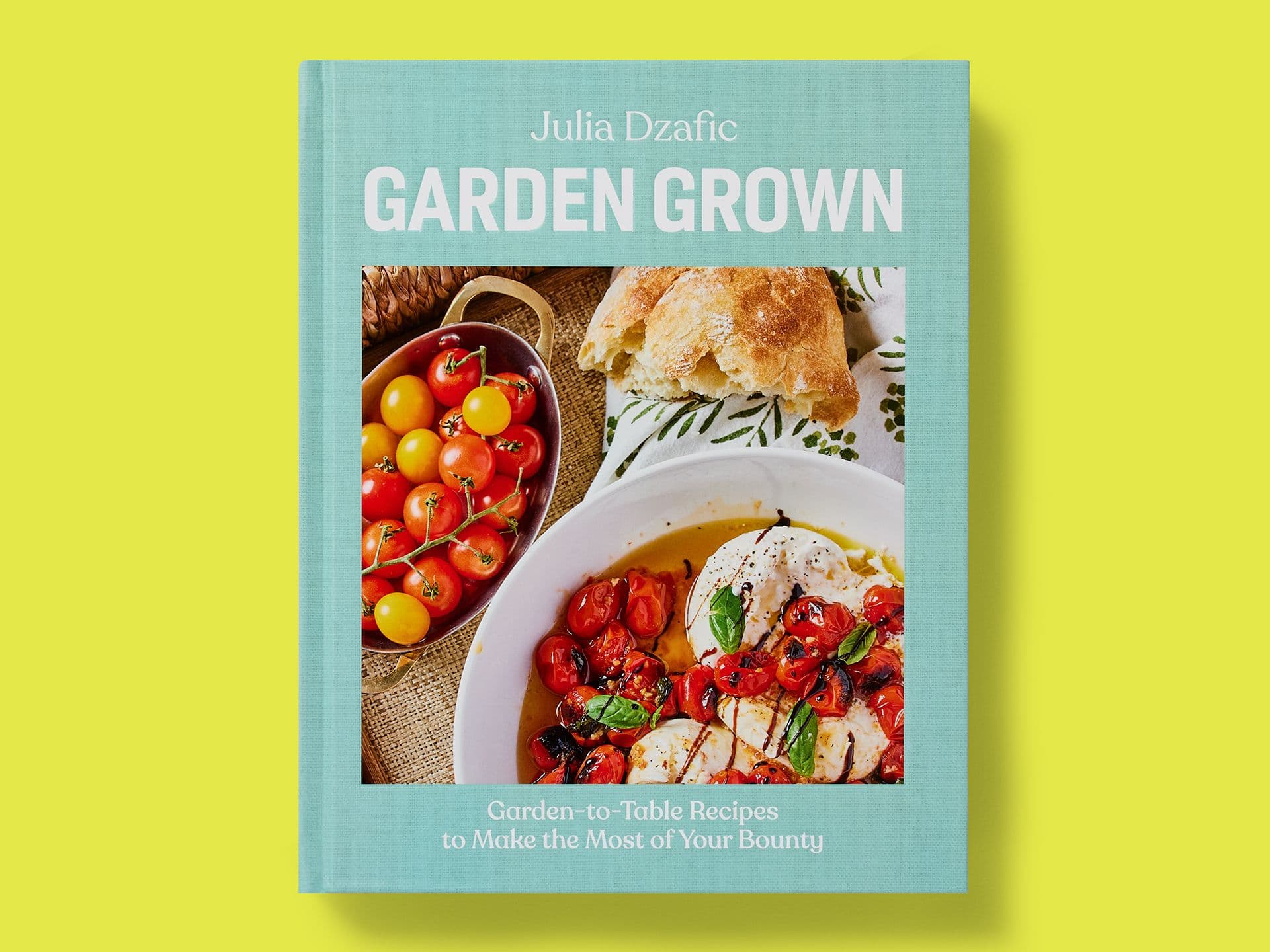Light blue book cover titled "Garden Grown" by Julia Dzafic, featuring a food photograph of roasted tomatoes with burrata, fresh cherry tomatoes in a bowl, and crusty bread, with the subtitle "Garden-to-Table Recipes to Make the Most of Your Bounty," set against a yellow background.