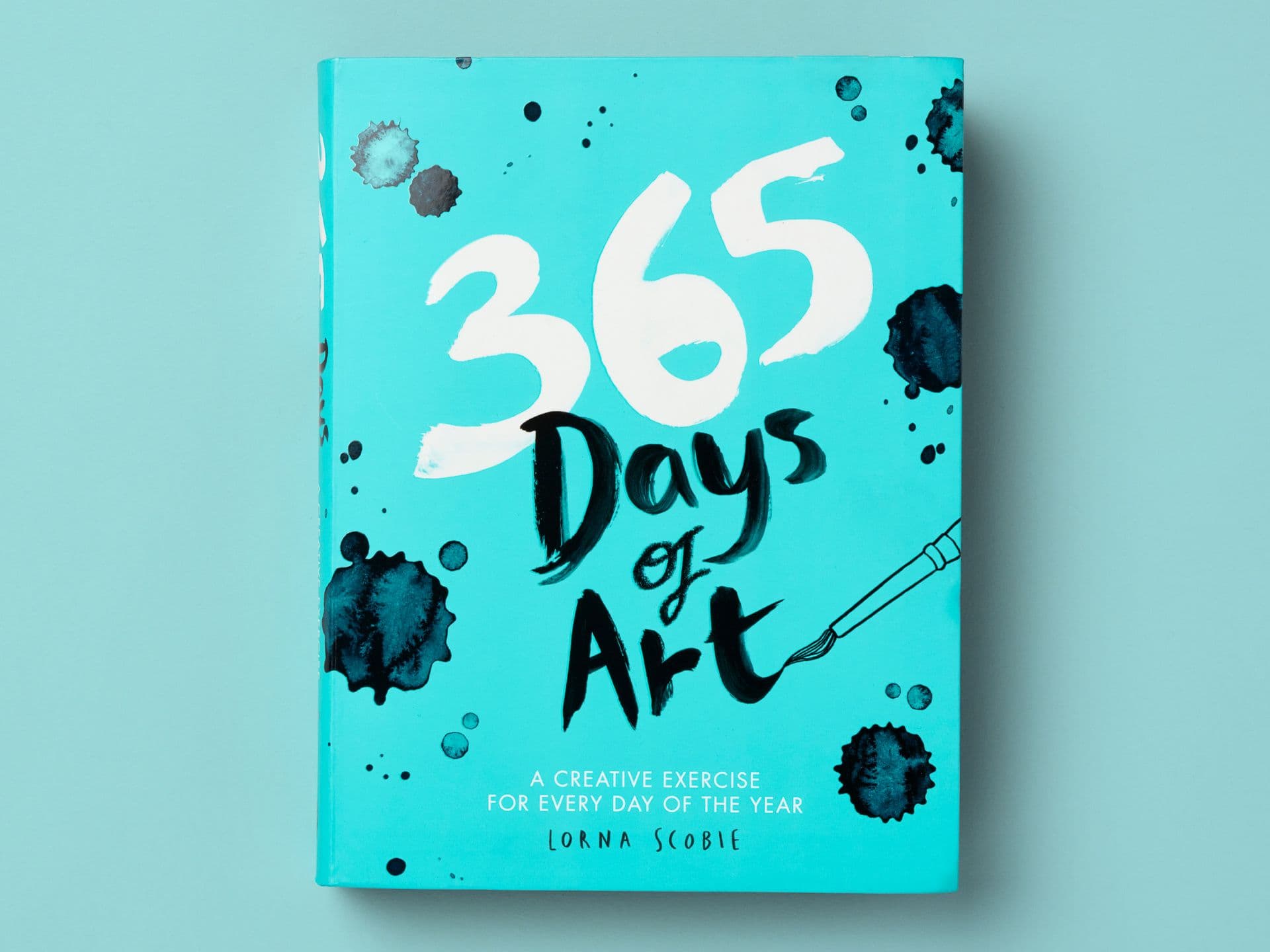 Book titled "365 Days of Art" on a turquoise background, featuring bold hand-painted lettering and black ink splatter illustrations, with a small paintbrush graphic on the right. Subtitle reads "A creative exercise for every day of the year," with the author's name, Lorna Scobie, at the bottom.